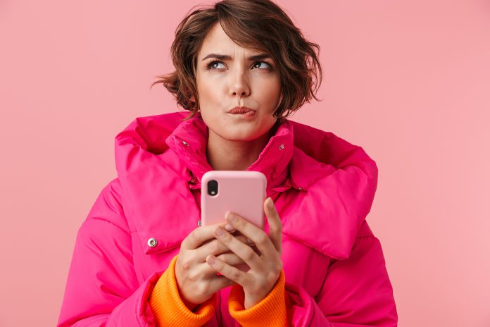 Portrait of young thinking woman using cellphone and looking upw