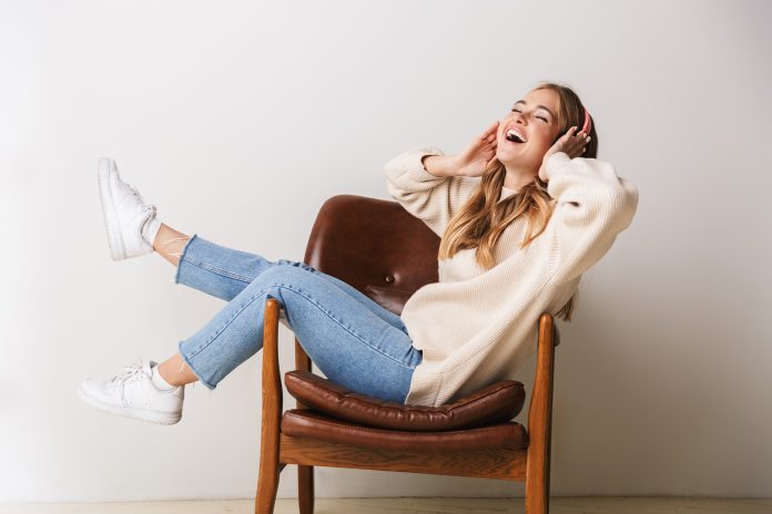 Image of excited young woman smiling and using headphones while