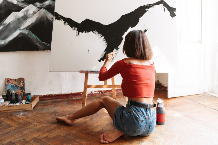 Portrait of young woman using painting tools while drawing in st