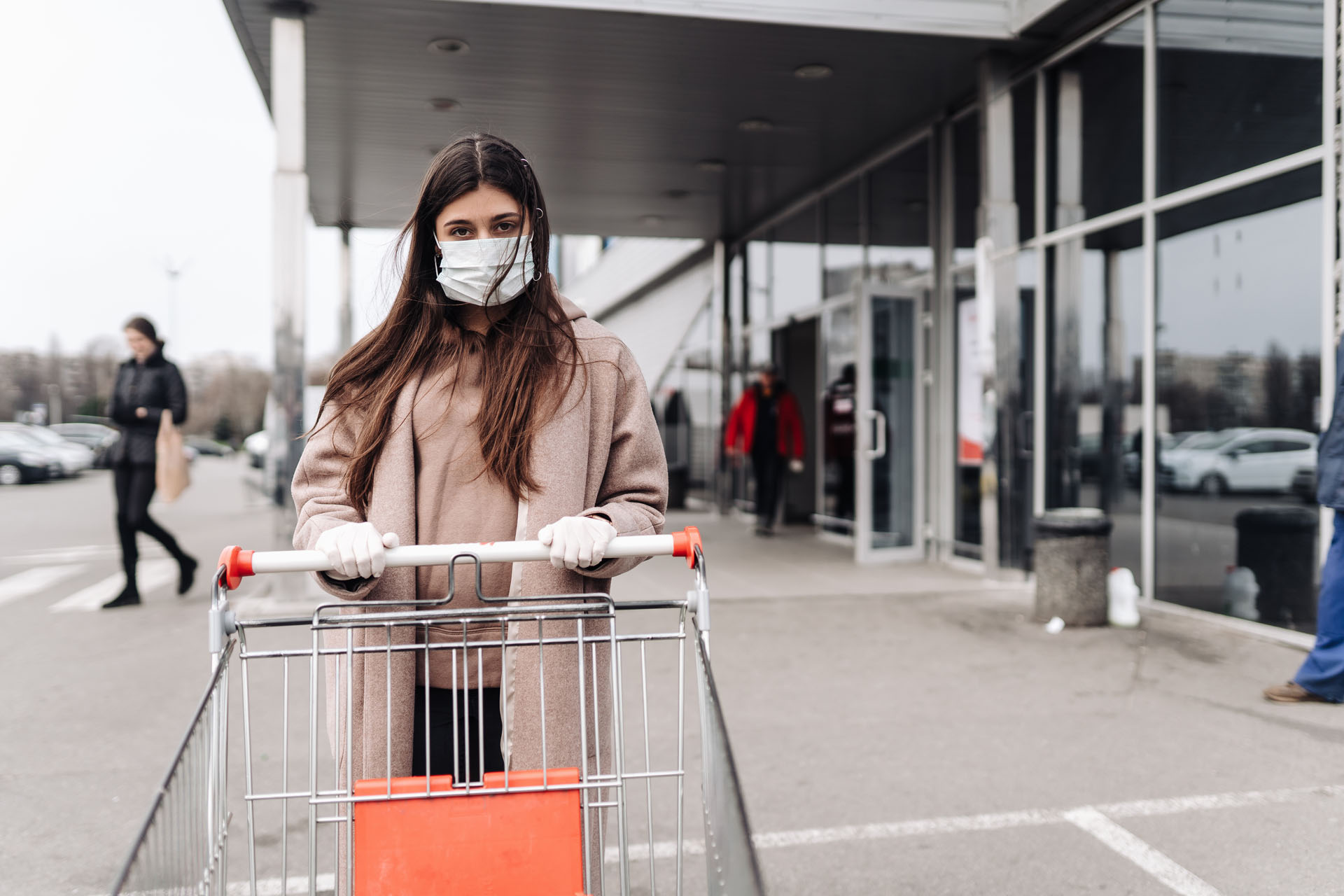 Young woman wearing protection face mask against coronavirus 2019-nCoV pushing a shopping cart.